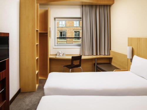 a room with two beds and a desk and a window at ibis Nottingham Centre in Nottingham
