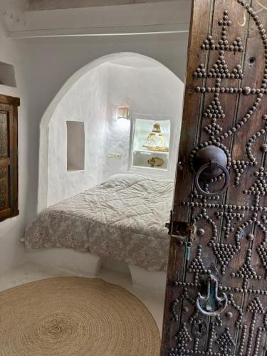 a room with a small bed in a room with a door at Hoûch Les Anartistes in Erriadh