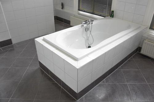a white bath tub in a white tiled bathroom at Hotel Nieuwe Markt in Deventer
