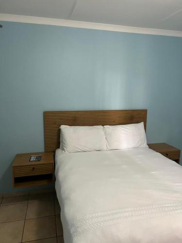 a bedroom with a white bed with a wooden headboard at Masakwe BNB in Soweto