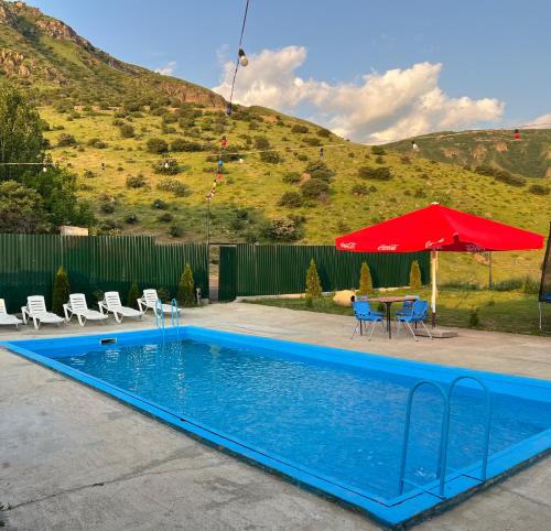 a swimming pool with a table and a red umbrella at Bardzunq Garden Resort in Goghtʼ