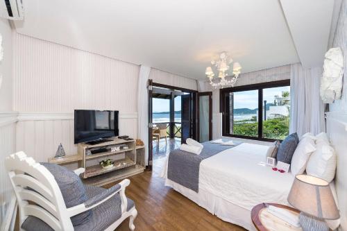 a bedroom with a bed and a tv and some chairs at Refúgio das Galés Mariscal in Bombinhas
