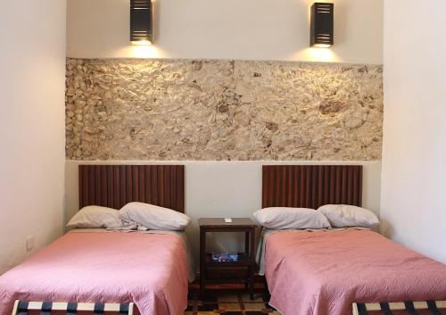 a room with two beds with pink covers and a stone wall at House with pool in downtown Merida, Yucatan in Mérida