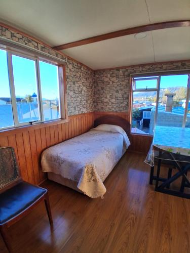 a bedroom with a bed and a table and windows at Cabaña León in Puerto Natales
