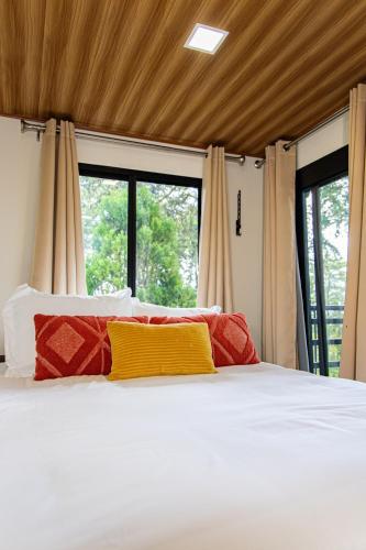 a bed with red and yellow pillows in a room with windows at Casa Bajareque in Cerro Punta