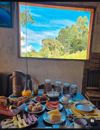 a table topped with plates of food and a window at Chalé vale do Monte Verde in Camanducaia