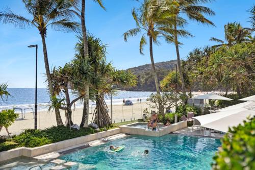 ein Swimmingpool neben einem Strand mit Palmen in der Unterkunft Fairshore in Noosa Heads