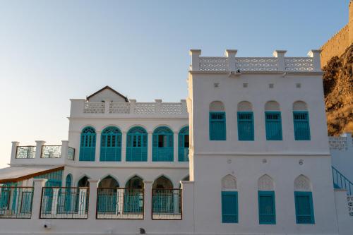 a white building with green windows next to a cliff at Al Bait Al Sharqi in Muscat
