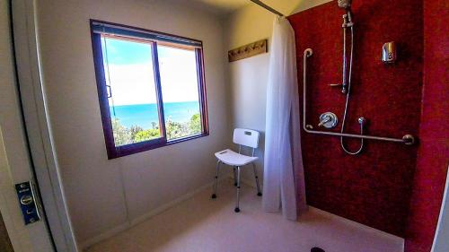 a bathroom with a shower and a window and a chair at Sunrise Apartment - Golden Bay in Onekaka