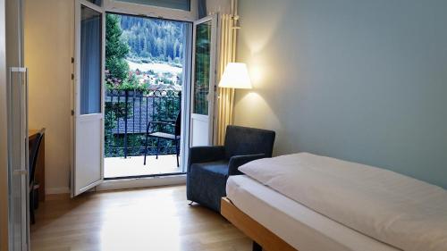 a bedroom with a bed and a chair and a large window at Hotel Fravi in Andeer
