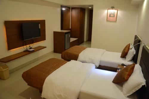 a hotel room with two beds and a flat screen tv at Hotel Yuvraj in Vadodara