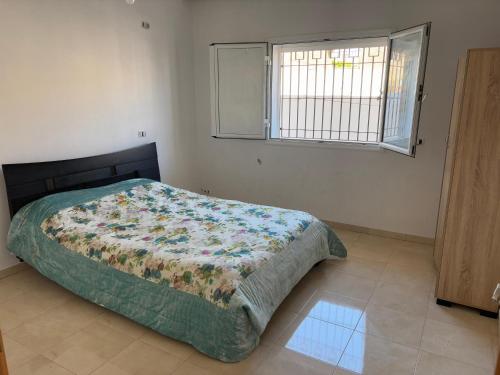 a bedroom with a bed with a comforter and a window at Villa blanche sfax in Sfax