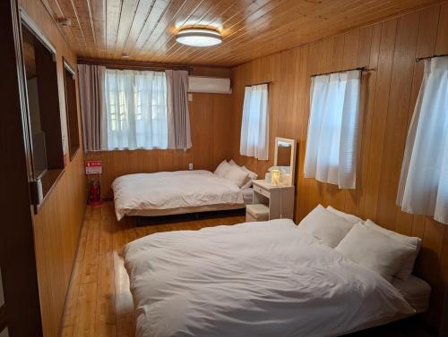 two beds in a room with wooden walls at Seasiders in Ichinomiya