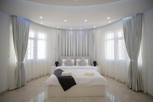 a bedroom with a large white bed with windows at Muscat Stays in Muscat