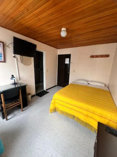 a bedroom with a yellow bed and a desk at Hotel Cordillera Real in Sogamoso