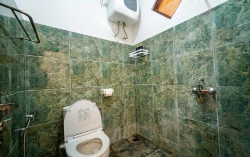 a bathroom with a toilet and a green tiled wall at Rumah Rini by Rumah Weda in Ubud