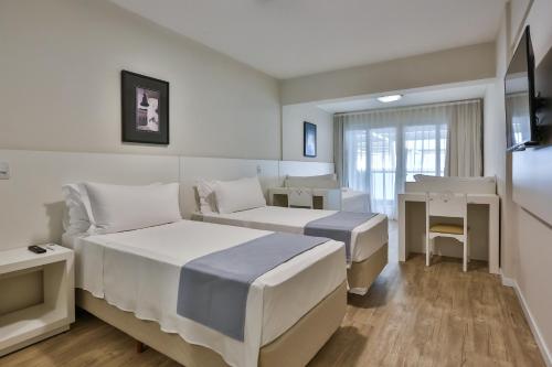 a hotel room with two beds and a desk at Itapema Beach Hotel & Convention in Itapema