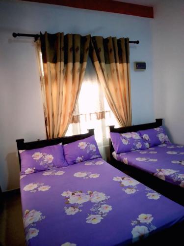 a bedroom with two beds with purple sheets and a window at New Dinu Holiday Inn in Kataragama