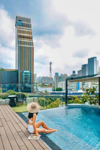 a woman in a hat sitting next to a swimming pool at Tastoria Collection Sukhumvit in Bangkok