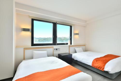 two beds in a room with two windows at First Inn Haiki in Sasebo
