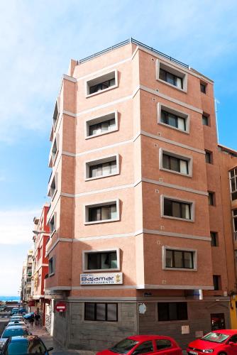 a tall brick building with cars parked in a parking lot at Hotel Apartamento Bajamar in Las Palmas de Gran Canaria