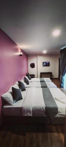 a row of beds in a room with a pink wall at City Hub Hotel Sitiawan in Sitiawan