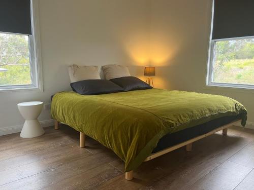 a bedroom with a bed with a green comforter and two windows at Happy Mountain House in Blackheath