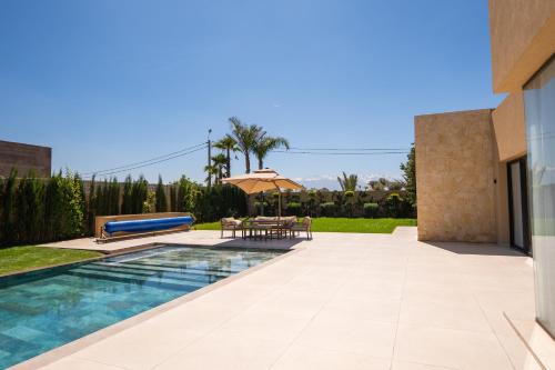 a swimming pool with a table and an umbrella at Villa prestige, terrain padel, salle de sport, hammam in Aït Amara el Ouled