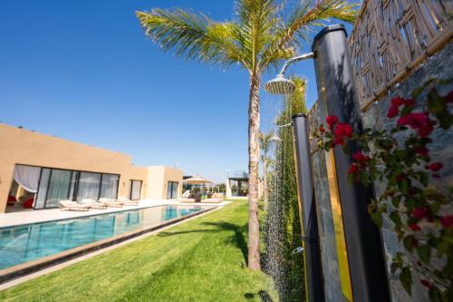a fence with a palm tree next to a swimming pool at Villa prestige, terrain padel, salle de sport, hammam in Aït Amara el Ouled
