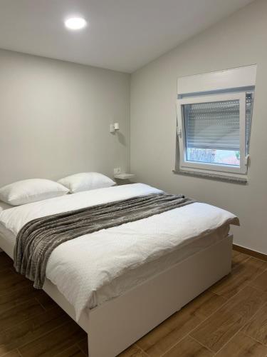 a white bedroom with a bed and a window at Apartman Lea in Sibinj