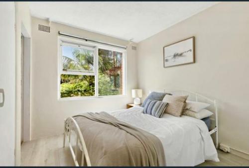 a white bedroom with a bed and a window at Footsteps to Freshwater Beach in Freshwater