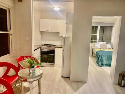 a small kitchen with a table and a room with a bed at Footsteps to Freshwater Beach in Freshwater