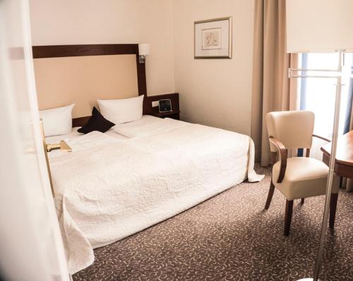 a bedroom with a white bed and a desk and a chair at Heerens Hotel in Emden