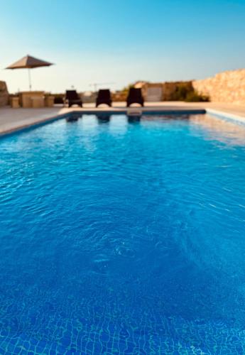 a blue swimming pool with chairs and an umbrella at Danny House in Nadur