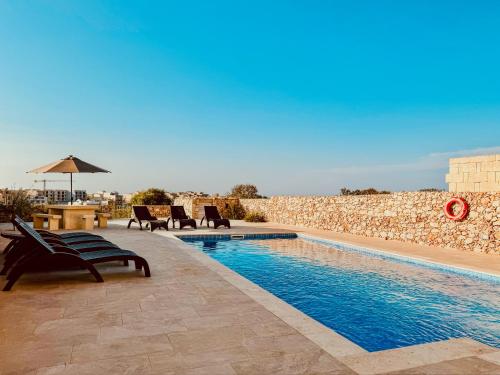 a swimming pool with lounge chairs and an umbrella at Danny House in Nadur