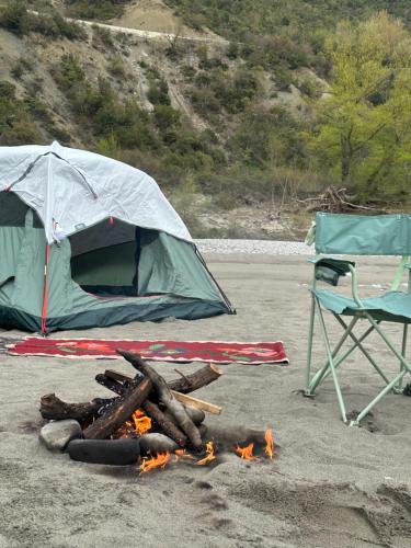 a tent and a chair on a beach with a fire at Wild Camping Vjosa in Përmet