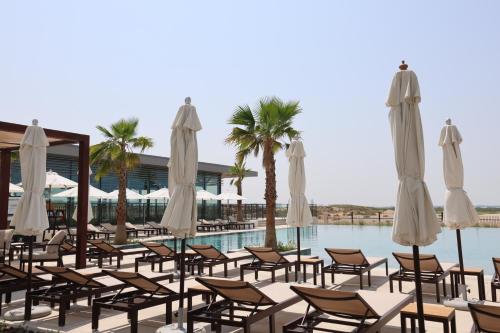 a group of chairs and umbrellas next to a pool at 1BR Yas Golf Collection, short walk to Water Park in Abu Dhabi