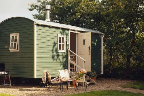 a green shed with two chairs and a table in front of it at Shepherd's Hut - Jasmine in Haverfordwest