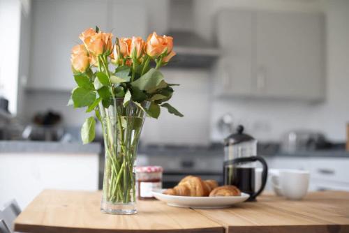 a vase of orange roses and a plate of bread at Cosy 3 Bed Near Beaches, Cardiff & Brecon Beacons in Coity