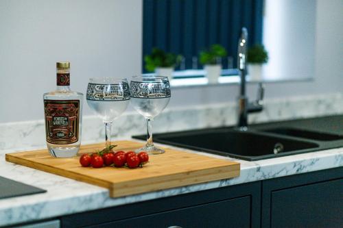a bottle of alcohol and two wine glasses on a cutting board at BOOTique House - Luxury Group Accommodation for 12 in Wakefield