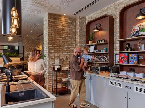 a man and a woman standing in a kitchen with a baby at Aparthotel Adagio London City East in London