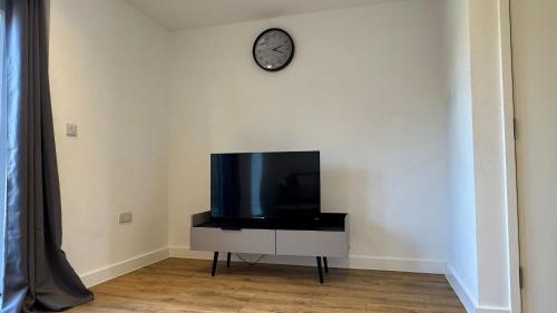 a living room with a flat screen tv on a wall with a clock at Joyful Management - A Mordern Semi-Detached House with 3 bedroom in Manchester