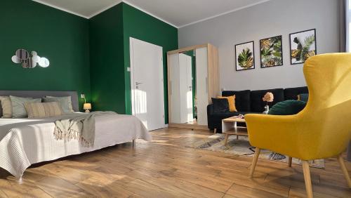 a bedroom with green walls and a bed and a yellow chair at Studio - Apartamenty Parkowe in Gniezno