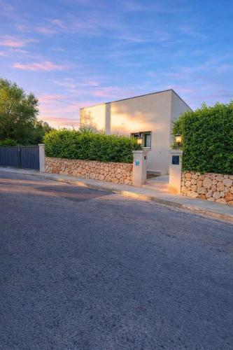 a white building with a stone wall next to a street at Casa Baleares TS SL in Cala Santanyi