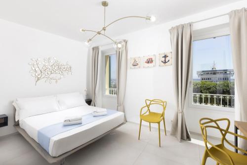 a white bedroom with a bed and a yellow chair at Domo Cicindela Boutique Rooms Centro Carloforte in Carloforte