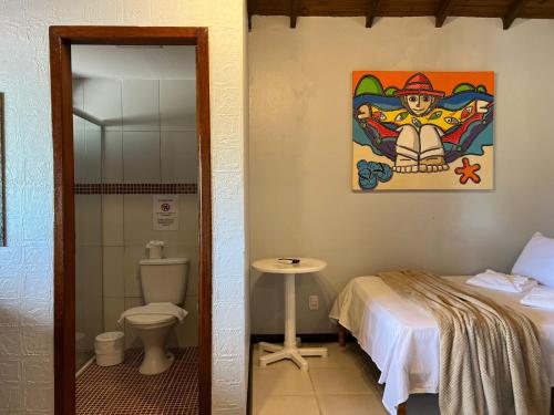 a room with a bed and a toilet and a painting at Pousada Kauai in Praia do Rosa