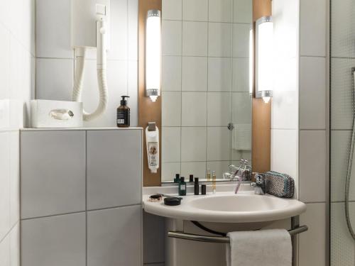 a white bathroom with a sink and a mirror at Ibis Sion in Sion