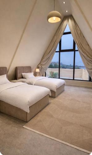 two beds in a room with a large window at اكواخ ساوثرنز in Ḩaḑram