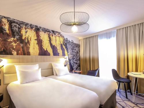 a hotel room with two beds and a painting on the wall at Mercure Cavaillon in Cavaillon