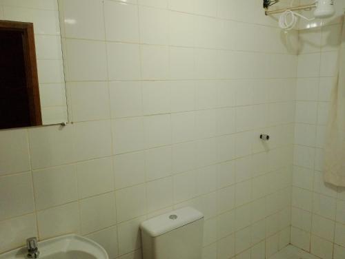 a white tiled bathroom with a toilet and a sink at Luz da Serra Hospedagens in Santana do Riacho